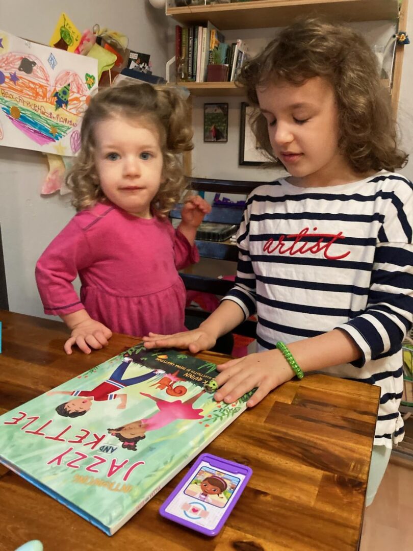 Two little girls looking at the JAZZY AND KETTLE story book